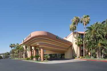 Daytime View of Hotel Exterior, Signage and Circle Drive Surrounded by Palm Trees