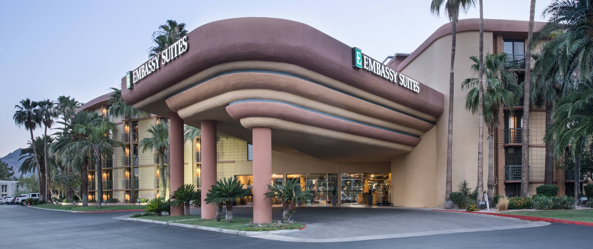 View of Hotel Exterior, Signage and Circle Drive Surrounded by Palm Trees at Dusk