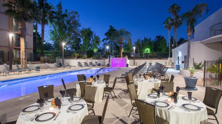 Mesas y sillas del restaurante junto a la piscina con vista de las palmeras