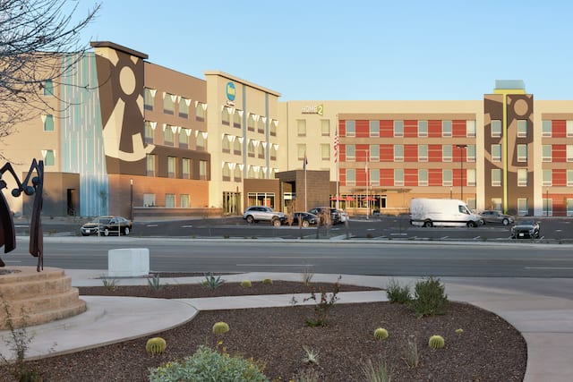 Modern dual property Home2 Suites and Tru hotel exterior with large parking lot and statue.