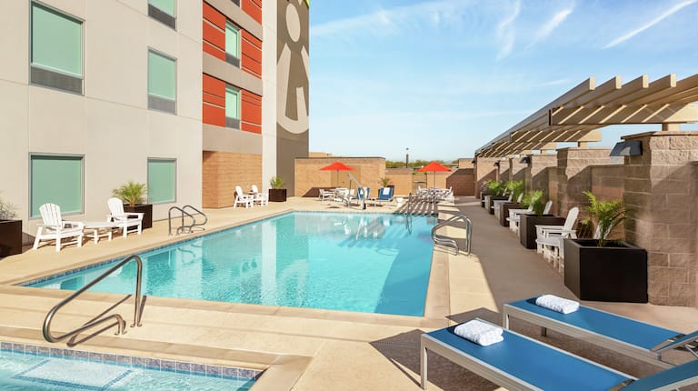 Large outdoor swimming pool featuring accessible chair lift, chaise lounge chairs, and patio tables with umbrellas.