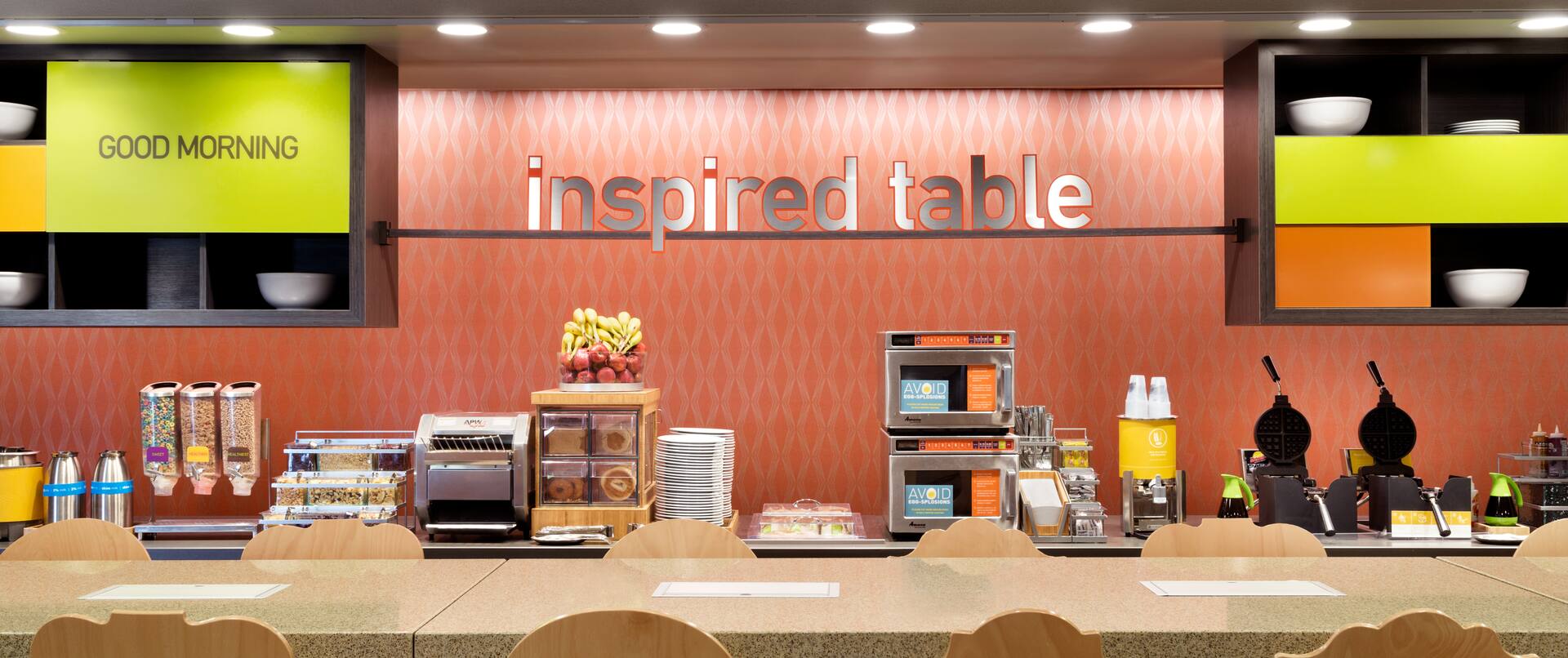 Brightly Lit Signage Above Food Service Area and Seating at a Community Table in Breakfast Dining Area