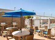 Daytime View of Two Grills by Brick Wall, Chairs, Tables With Blue Umbrellas on Outdoor Patio
