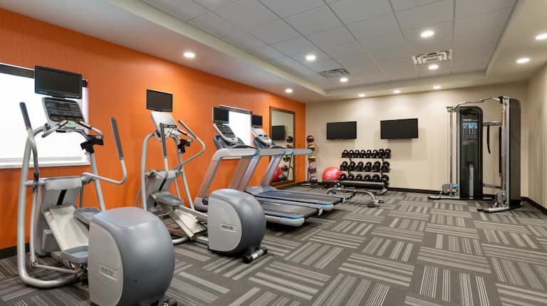 Fitness Area of Spin2Cycle With Cardio Equipment Facing Windows, Large Mirror, Weight Balls, Two TVs, Red Exercise Ball, Free Weights, and Weight Machine