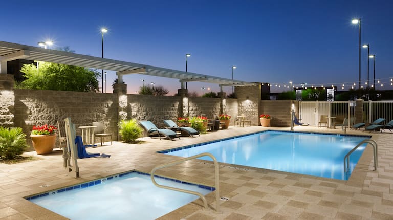 Illuminated Outdoor Pool and Hot Tub With Tables, Chairs,  Loungers and Plants at Night