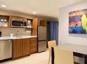 Suite Kitchen Featuring Artwork Over Dining Table, Wood Cabinets, Dishwasher, Microwave and Fridge