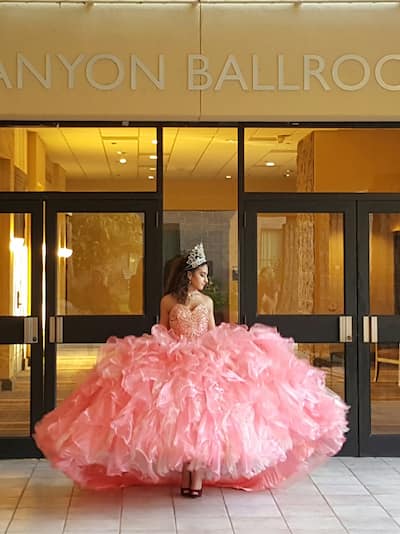 Une jeune fille heureuse debout à côté de l'entrée de la salle de réception Canyon, portant une robe rose pour Quinceañera