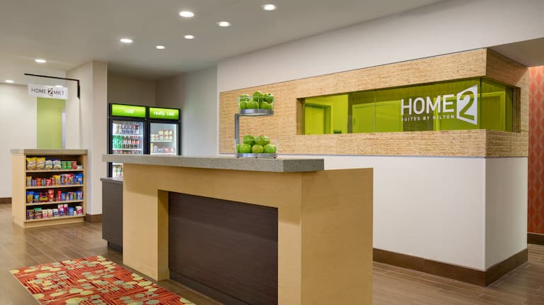 Green Hotel Sign Behind Front Desk With Green Apples on the Counter and  Signage Above Home2Market Items For Sale