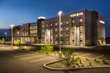 Angled View of Illuminated Hotel Exterior With Signage, Flagpole, Entrance, Landscaping, and Parking Lot at Night