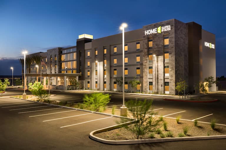 Angled View of Illuminated Hotel Exterior With Signage, Flagpole, Entrance, Landscaping, and Parking Lot at Night