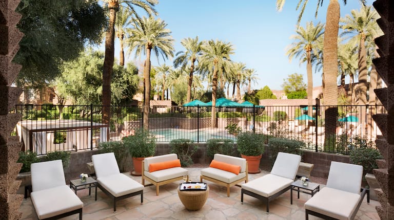 Deux chaises et quatre chaises longues sur le patio de la suite présidentielle avec vue sur la piscine entourée de palmiers 