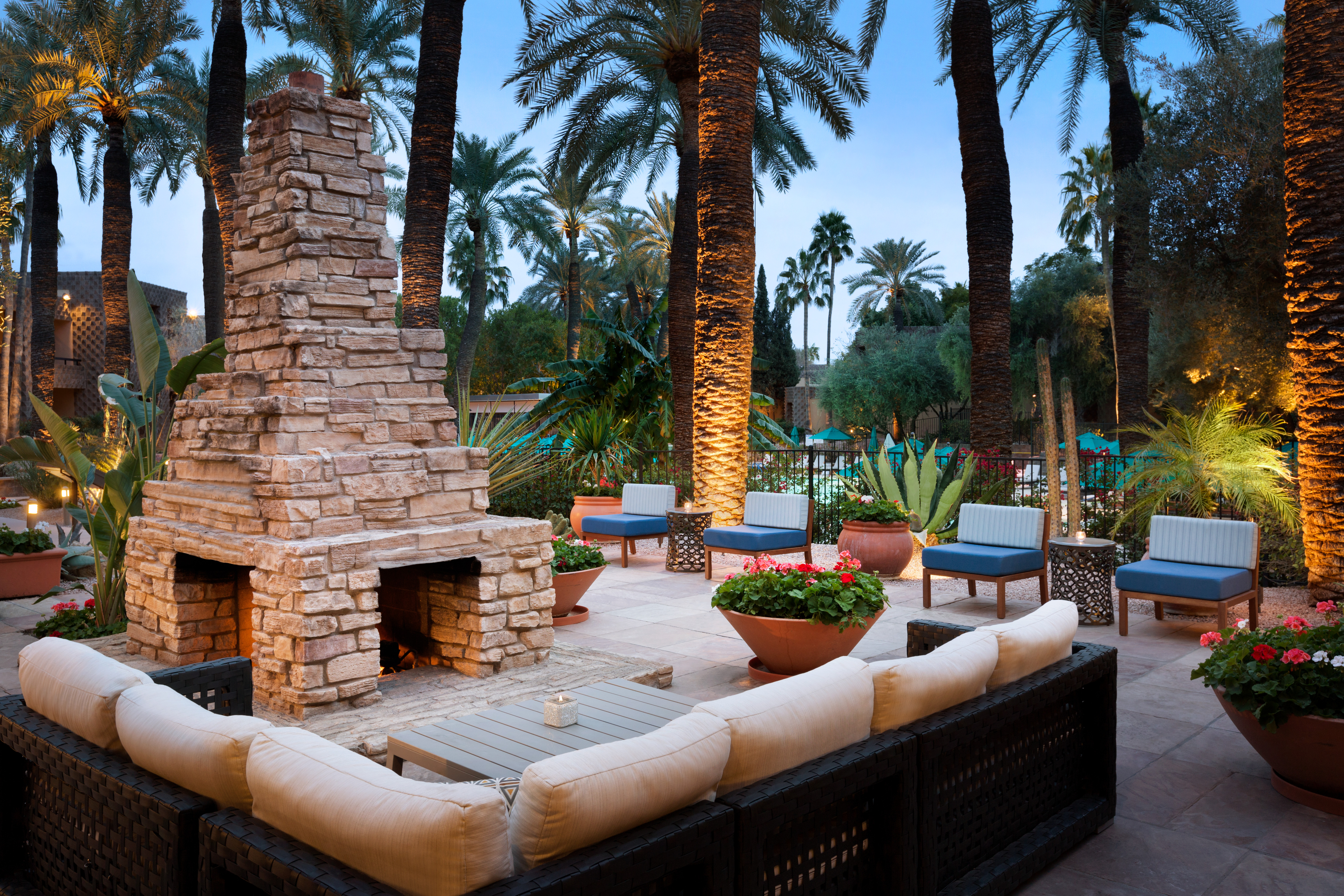 Illuminated Outdoor Patio With Furnace, Candlelit Tables, and Mixed Seating Surrounded by Palm Trees at Dusk