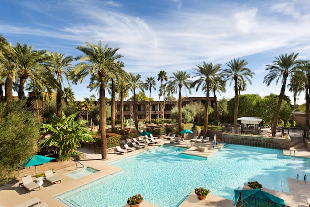 Daytime View of Green Sun Umbrellas, and Loungers by North Outdoor Pool Surrounded by Palm Trees and Hotel Exterior in Background