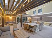 Outdoor patio area with sofas, coffee tables, chairs, and BBQ grills under pavilion with stringed lights