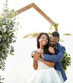 A smiling bride and groom embracing underneath a wedding arch. 