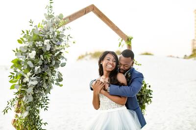 A smiling bride and groom embracing underneath a wedding arch. 