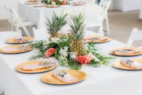 A wedding table set up with a flower arrangement and pineapples in the center 