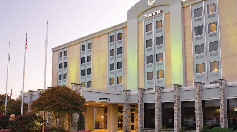 Angled View of Illuminated Hotel Exterior, Signage, Porte Cochère, Flagpoles, and Landscaping at Dusk