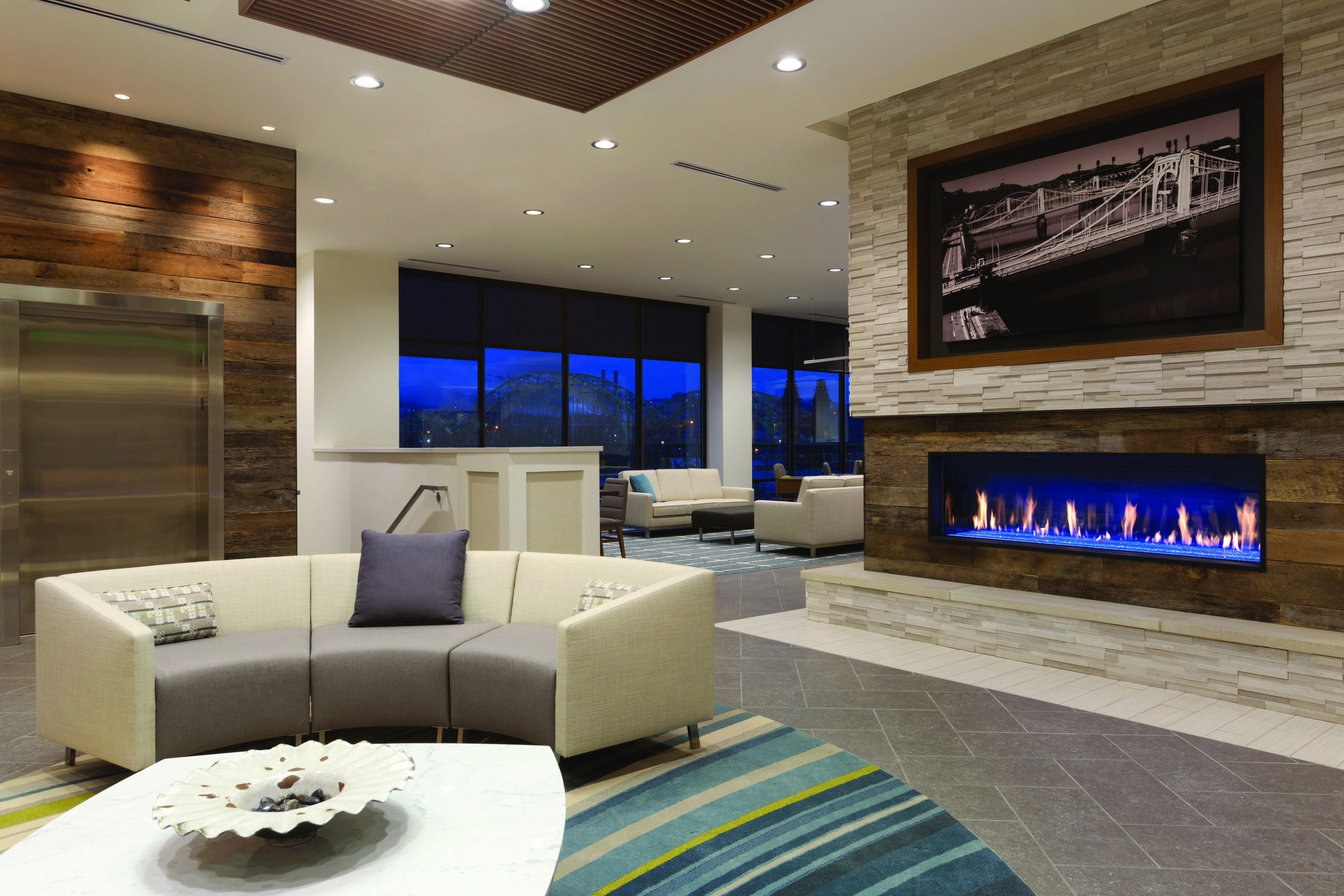 Lobby seating area with curved sofa, coffee table, and fireplace with art displayed above