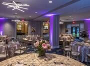 Purple Lighting, Place Settings, Flowers, Drinking Glasses, White Napkins, and Decorative Linens on Round Tables, Chairs, and Entry Doors in Ballroom