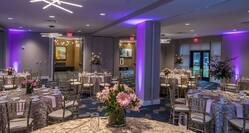Purple Lighting, Place Settings, Flowers, Drinking Glasses, White Napkins, and Decorative Linens on Round Tables, Chairs, and Entry Doors in Ballroom