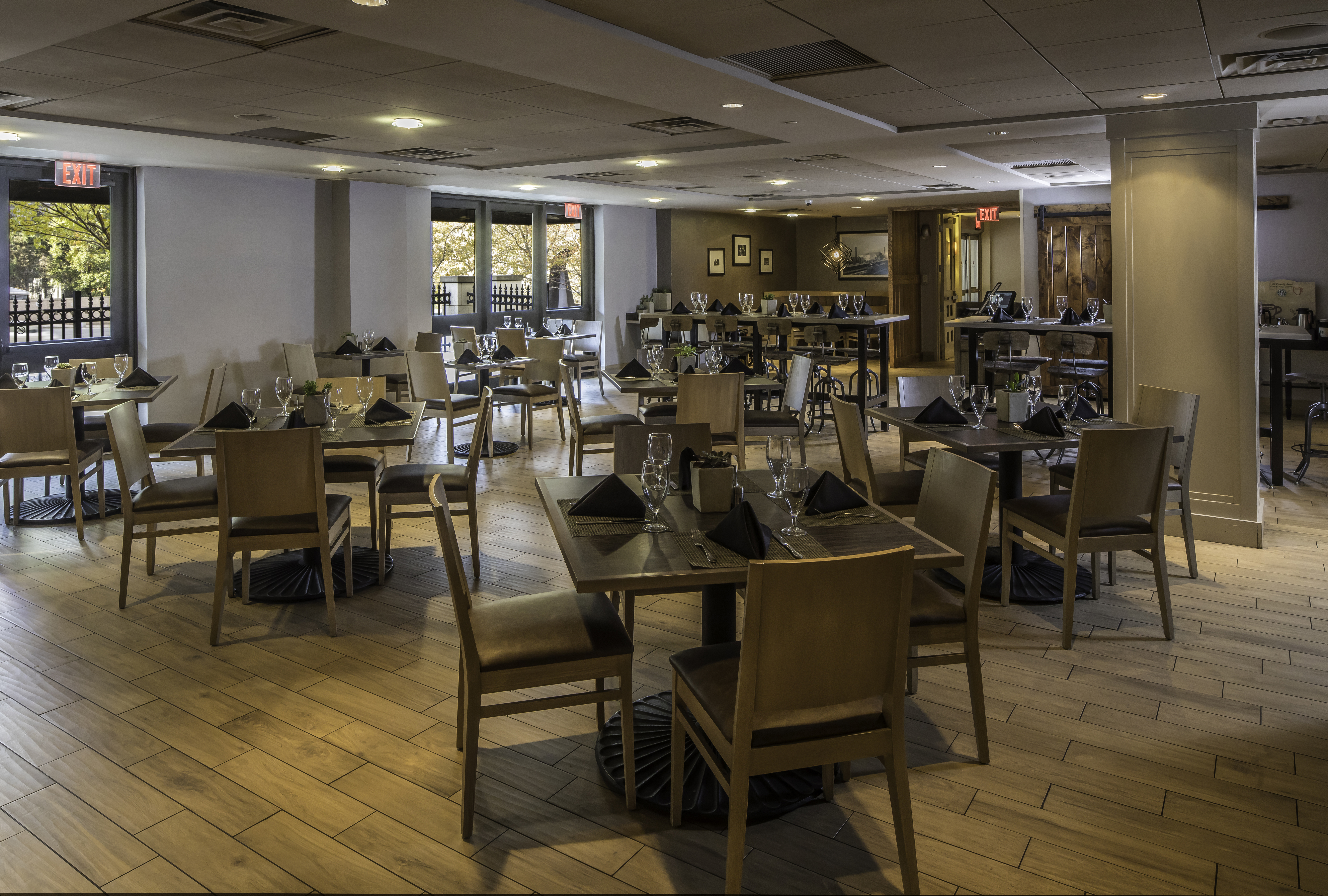 Windows, Glass Doors, Folded Black Napkins, Silverware, and Drinking Glasses on Dining Tables, Chairs, and Wall Art in Bigelow Grille