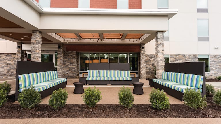 Daytime View of Outdoor Patio With Landscaping by Two Small Tables and Three Striped Sofas in Lounge Area