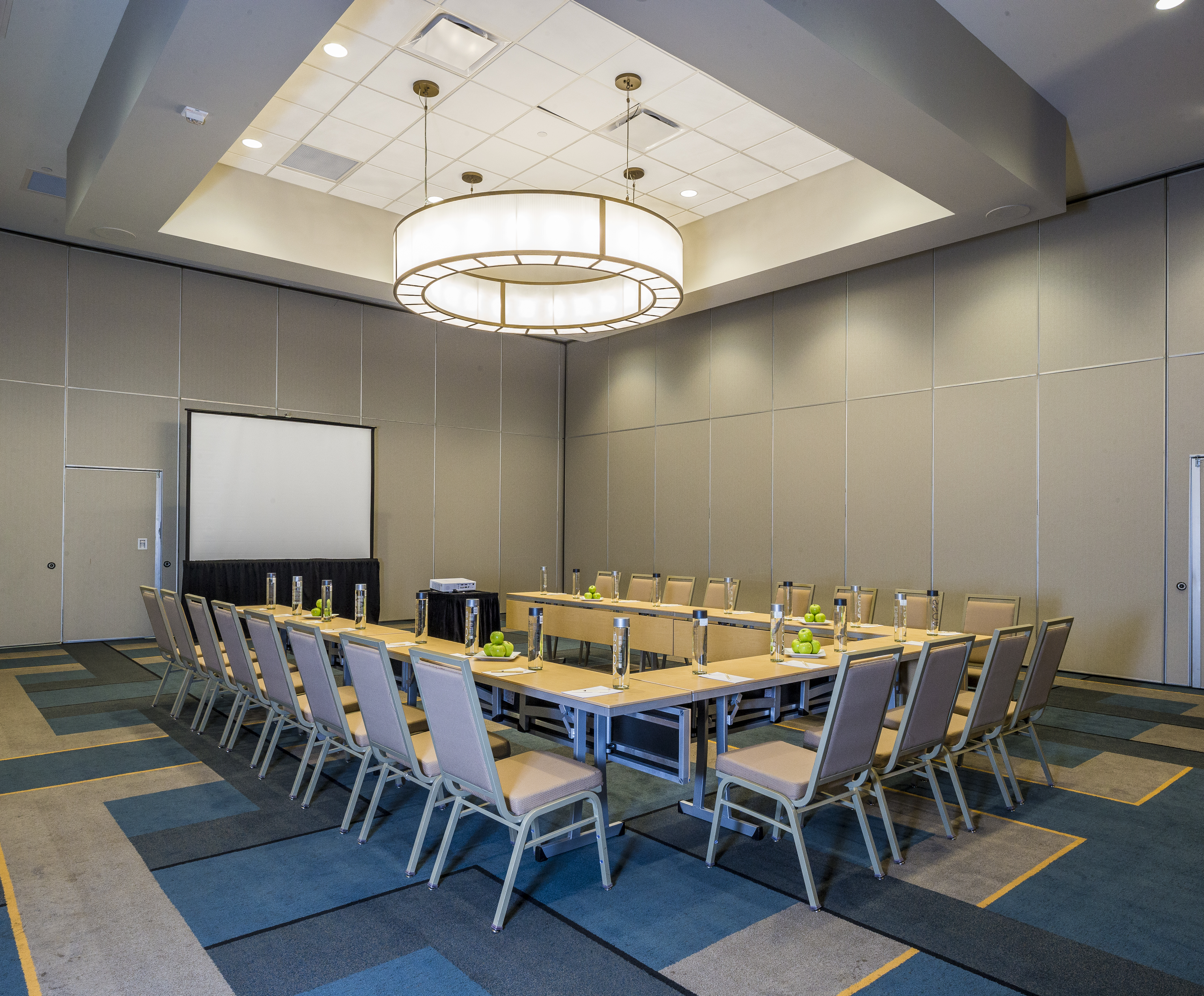 Meeting Room With Water Bottles and Bowls of Green Apples on U-Shaped Table, Chairs, Projector Table, and Presentation Screen