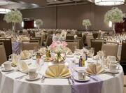  Place Settings, Fan Folded Napkins, Lavender Table Runners,  Candles, and Flowers on Dining Tables With White Linens, White Chairs in Banquet Hall Set Up For Wedding Reception