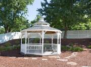 Outdoor gazebo surrounded by trees, shrubs, and white fence