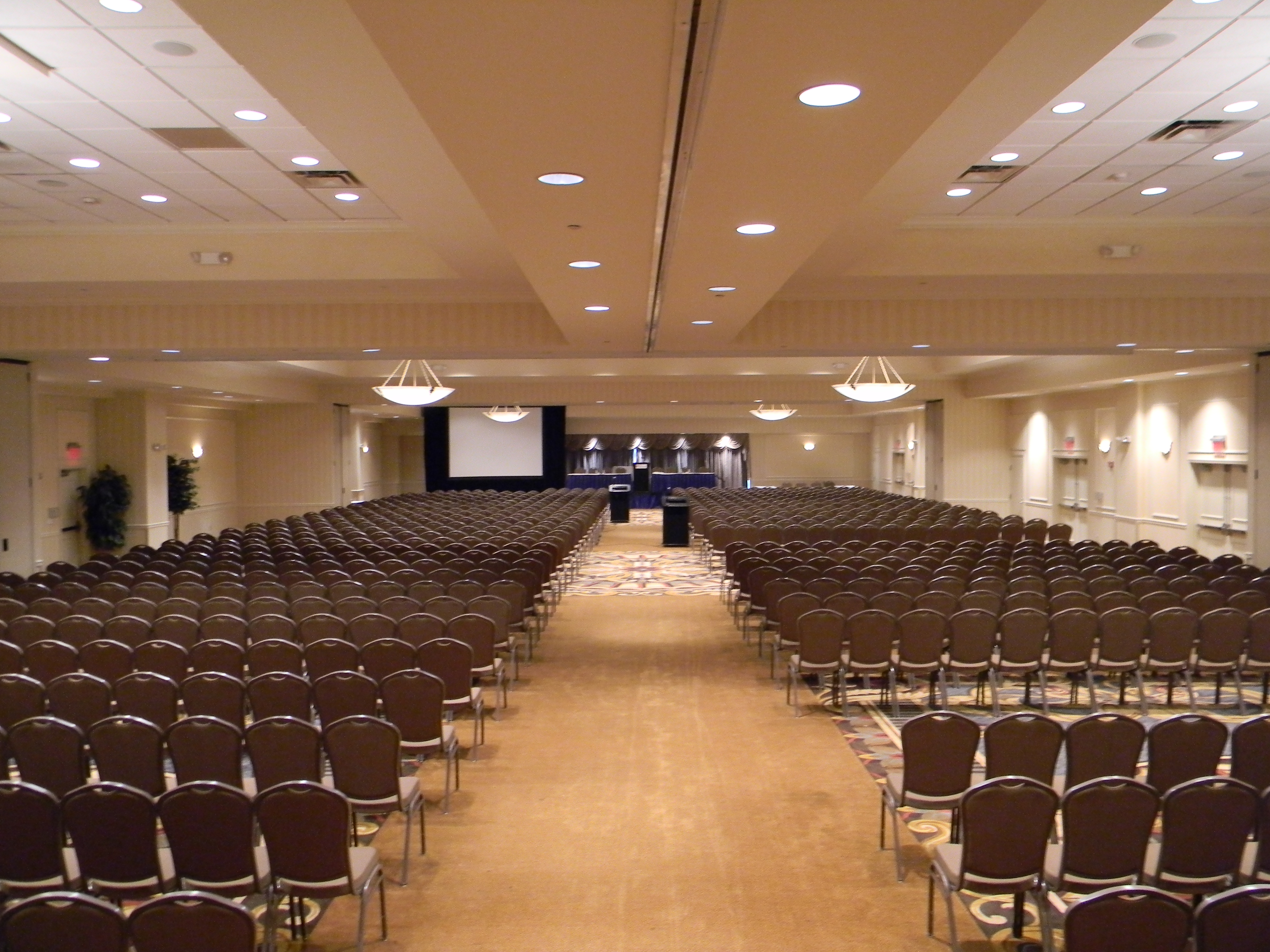 Grand Ballroom Arranged Theater Style With Rows of Chairs Facing Projector Screen and Stage