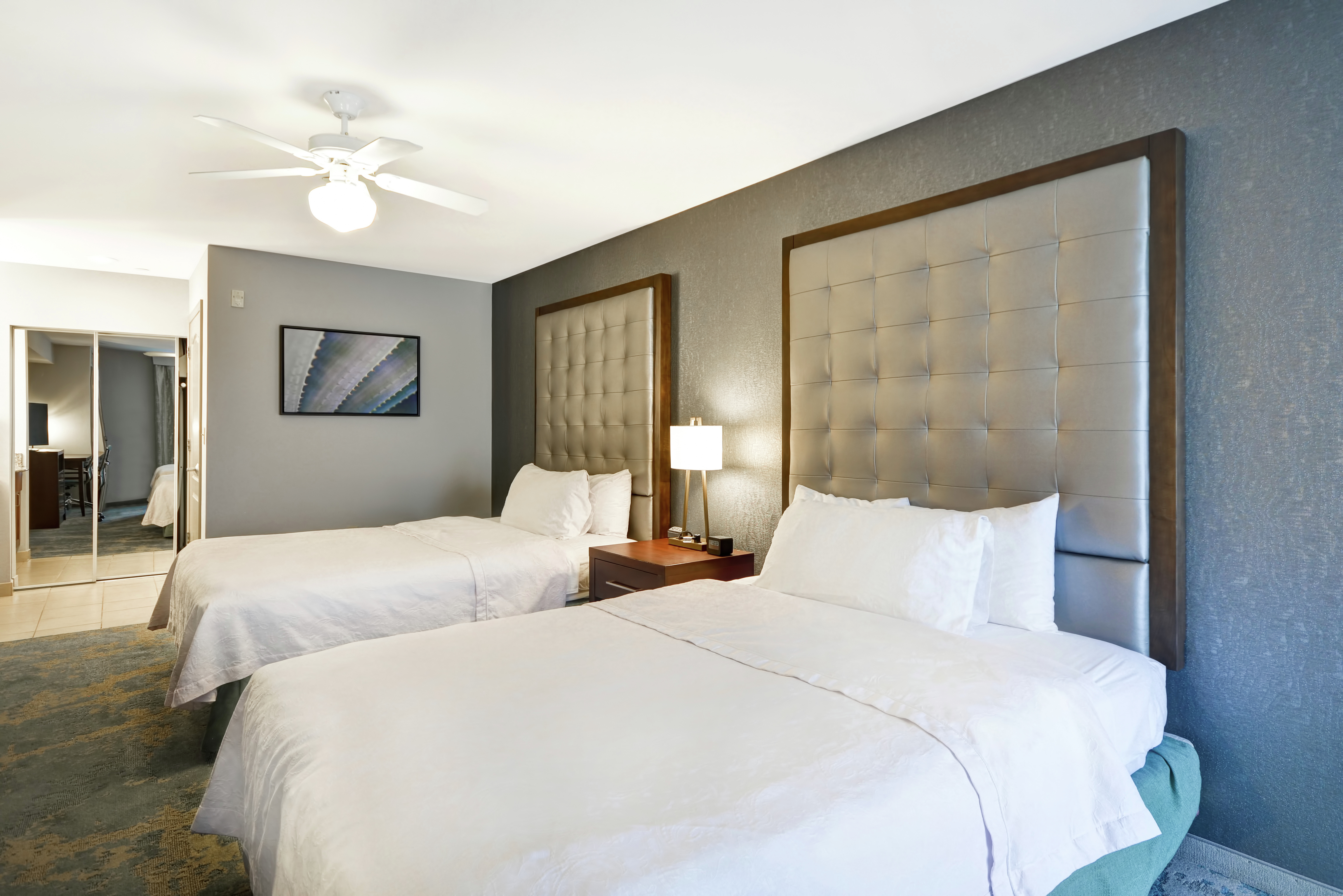 Ceiling Fan Above Two Queen Beds and Illuminated Lamp on Bedside Table in Guest Room