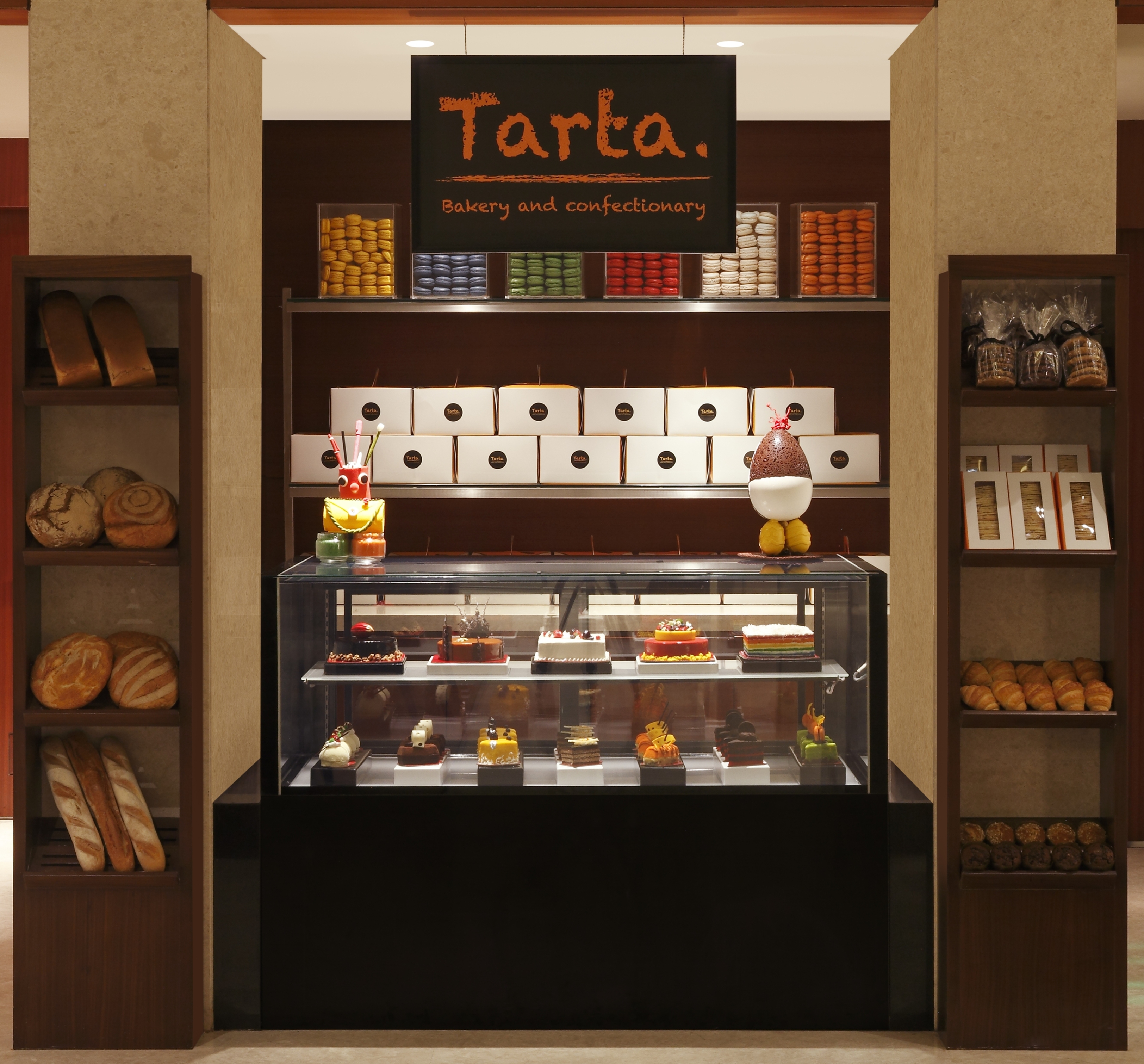 "Tarta Bakery and  Confectionary" Signage Above Display Case and Shelves With Baked Items For Sale