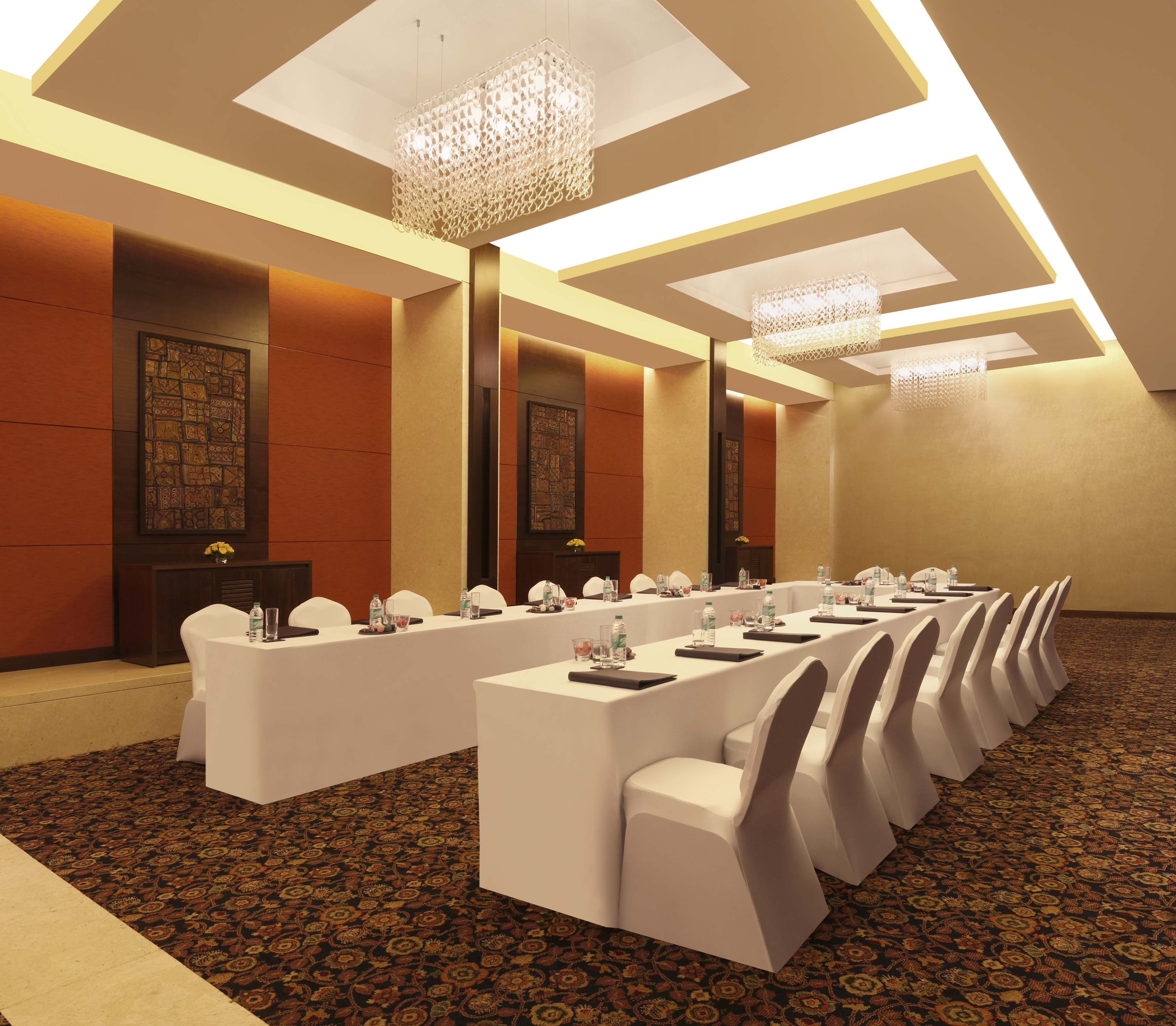 Vihara Banquet Hall With Wall Art, U-Shaped Table With Water Bottles, Notepads,  White Linens, and White Chairs