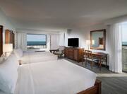 Two Queen Beds and Bedside Table Facing Beach View, Work Desk, TV and Reading Chair in Corner by Window