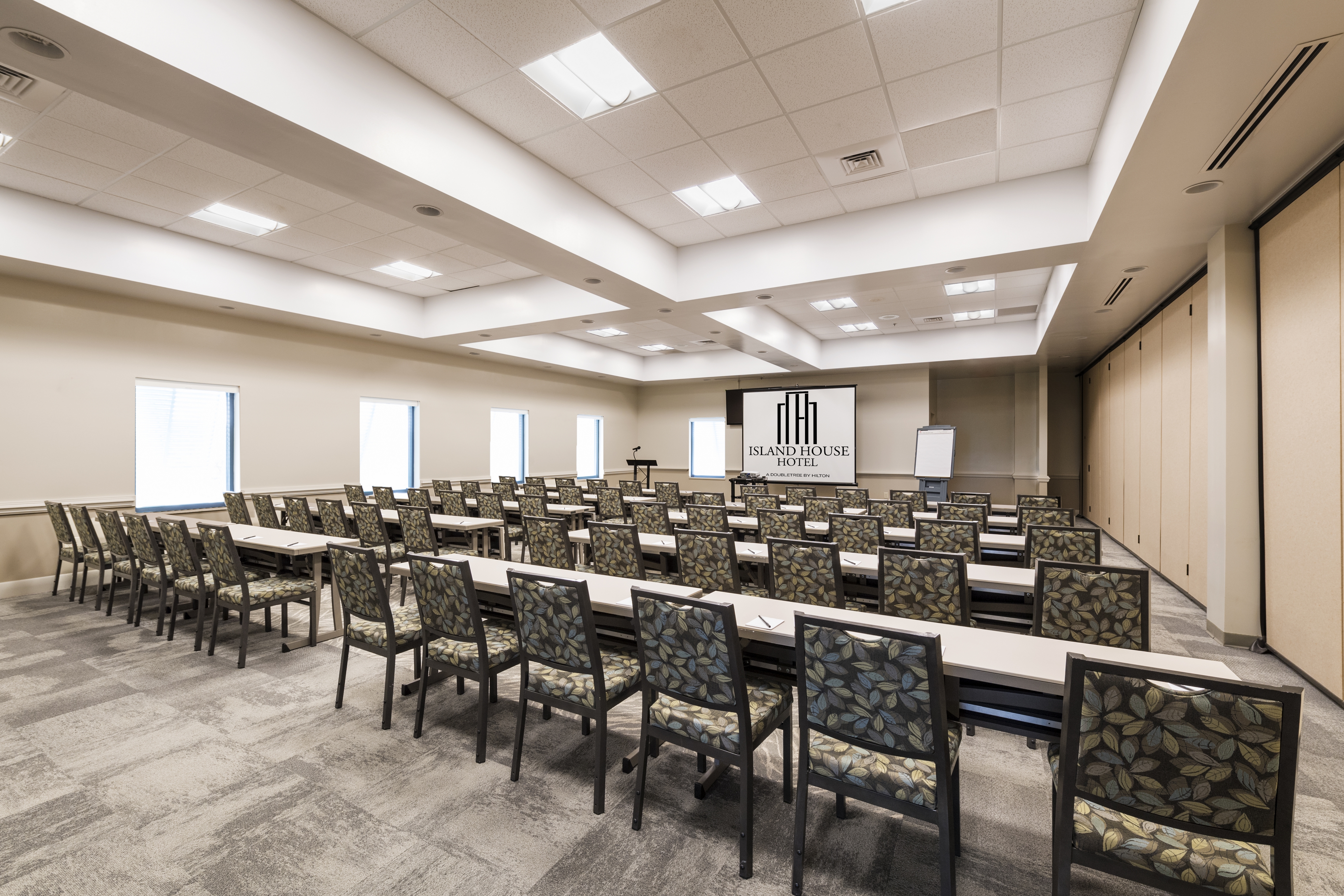 Ballroom in Classroom Setting with Long Tables and Chairs Facing Projector Screen with Outside Views