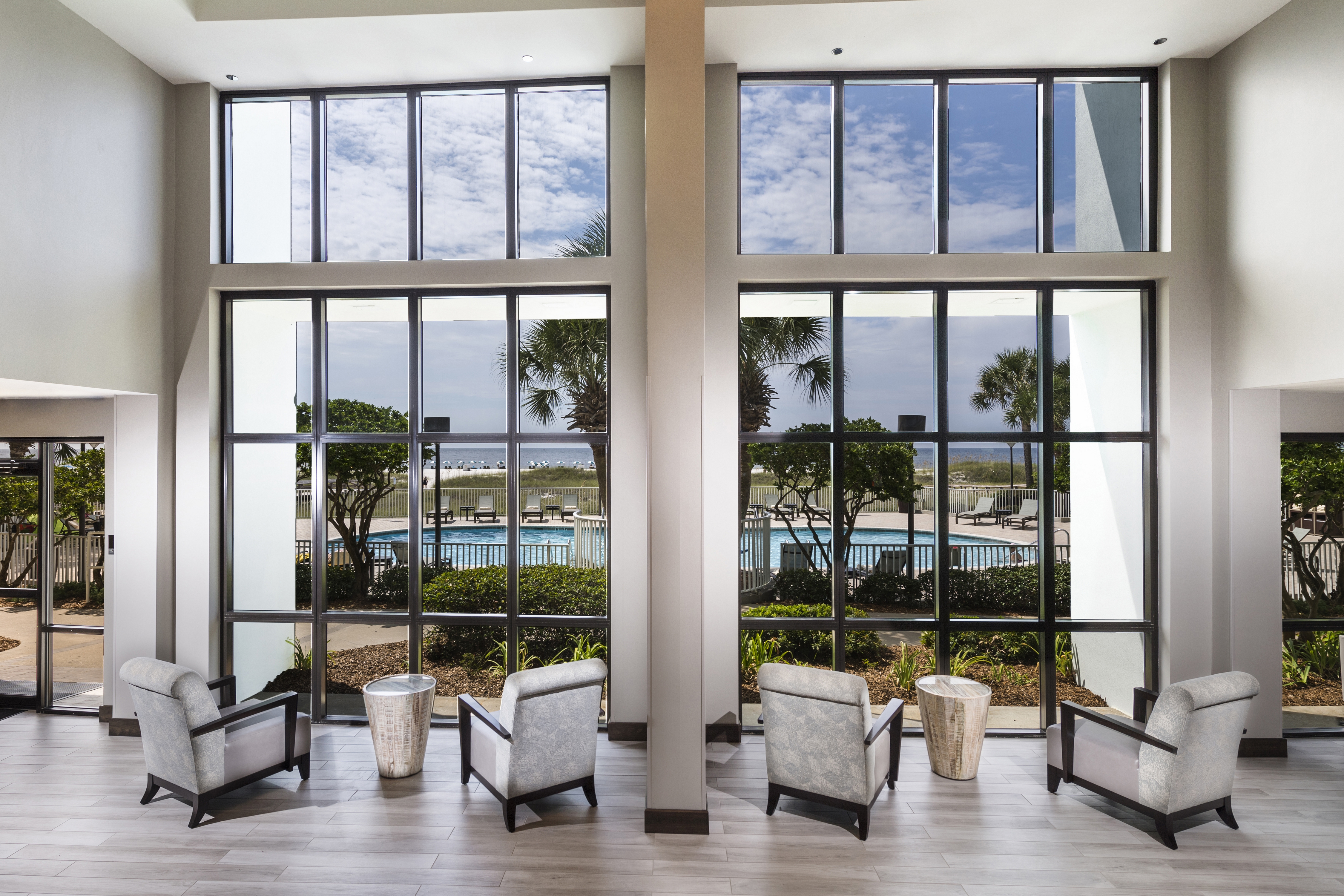 Rear View of Chairs and Tables in the Lobby that Face the Window with a View of the Pool and Beach