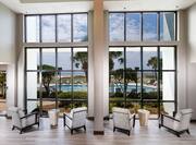 Rear View of Chairs and Tables in the Lobby that Face the Window with a View of the Pool and Beach