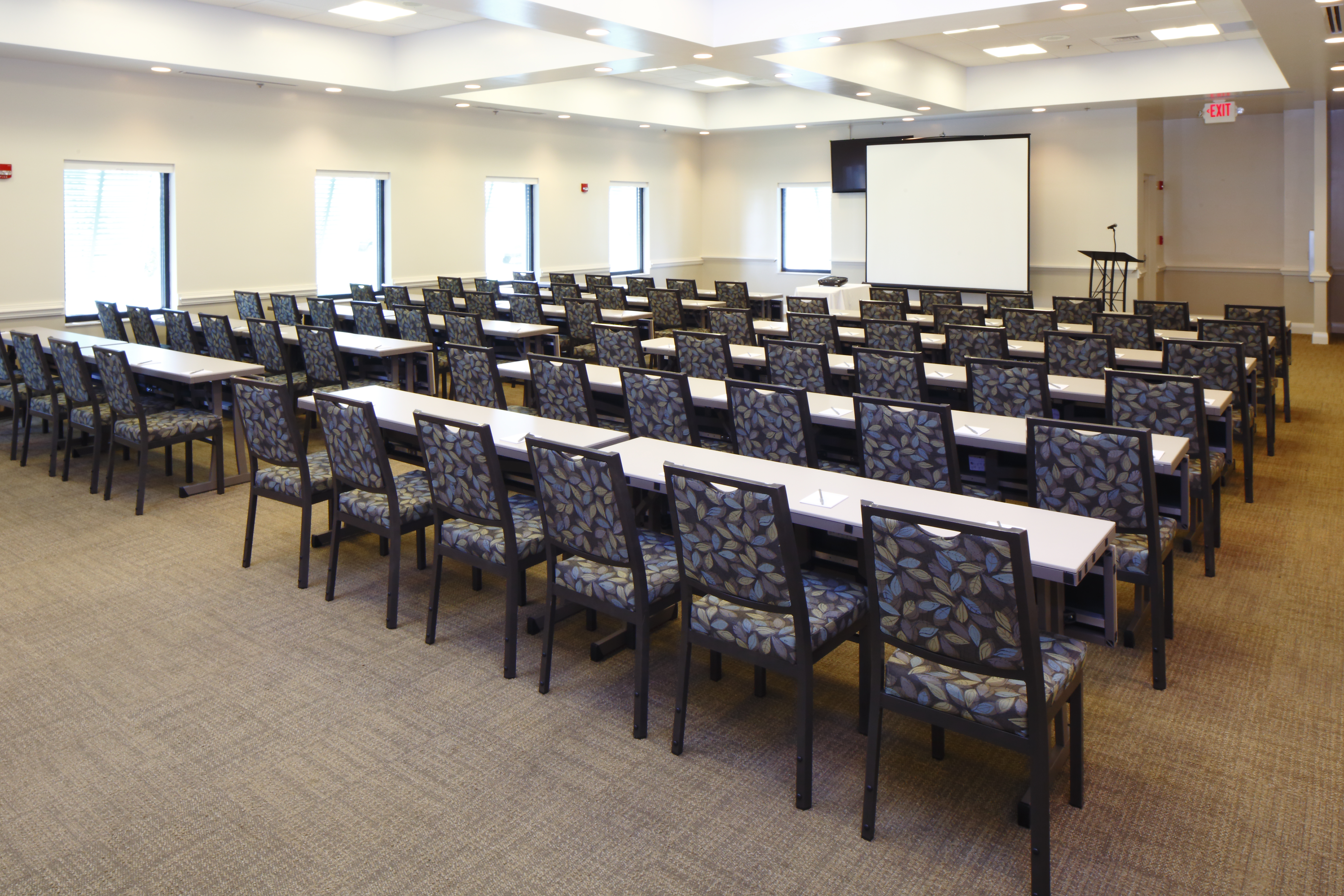 Classroom Setup in Meeting Room With Windows, Tables, Chairs, Presentation Screen, and Podium