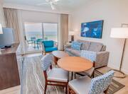 Junior suite living room with sofa, soft chair, coffee table, TV, small dining table with chairs, floor lamp, and balcony with gulf view
