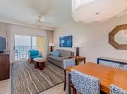 Suite living room with sofa, soft chair, coffee table, TV, dining table with chairs, and balcony with gulf view