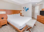 Suite with king bed, nightstands, lamps, footrest, and TV
