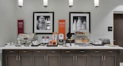 Breakfast serving area with buffet tray, oatmeal, pastries, waffle maker, and dining amenities
