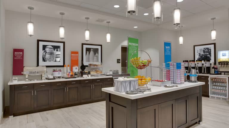 Breakfast serving area with buffet tray, coffee, juice, cereals, oatmeal, fruits, pastries, waffle maker, and dining amenities