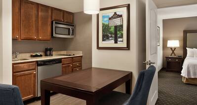 Spacious suite featuring fully equipped kitchen, dining table, and view into private bedroom with king bed.