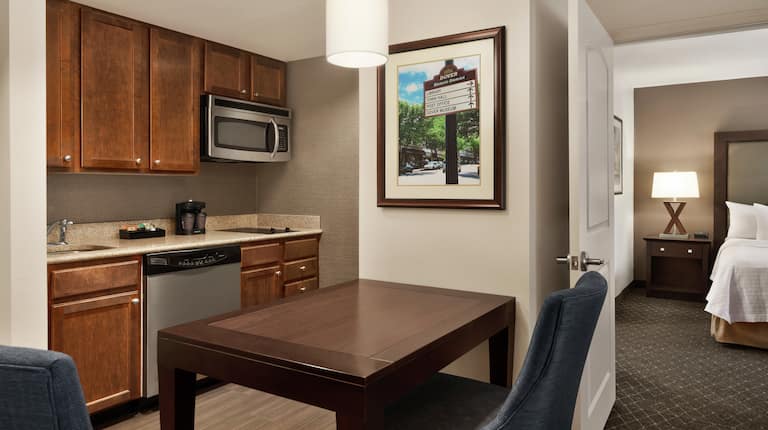 Spacious suite featuring fully equipped kitchen, dining table, and view into private bedroom with king bed.