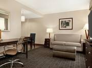 Spacious studio suite featuring lounge area with sofa, TV, and work desk with ergonomic chair.