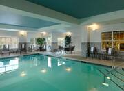 Indoor Pool with lounge chairs and dining table, and partial view of fitness center through indoor window