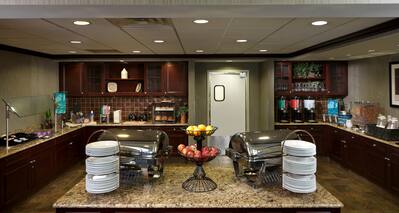 Breakfast serving area with buffet trays, coffee, juice, cereals, oatmeal, fruits, and dining amenities