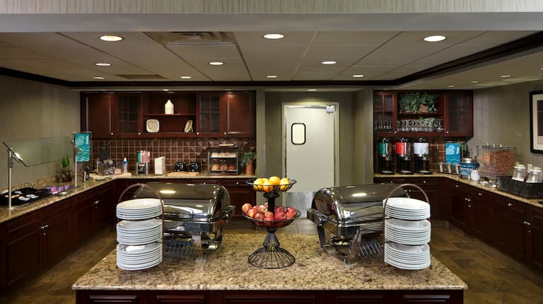 Breakfast serving area with buffet trays, coffee, juice, cereals, oatmeal, fruits, and dining amenities